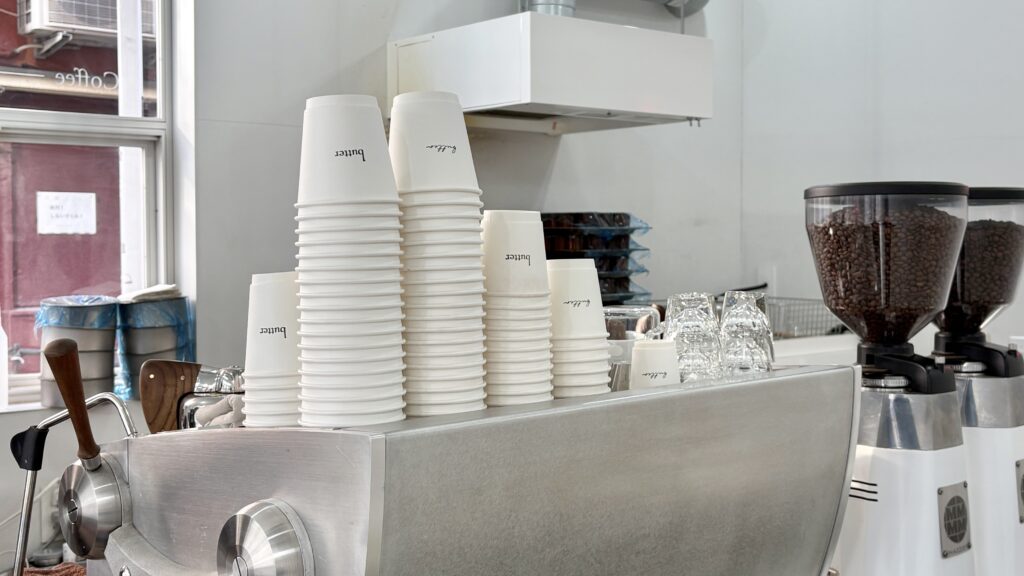 バターの白を基調とした無機質な店内にエスプレッソマシンとテイクアウトカップ